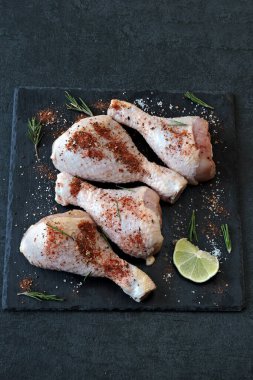 Koyu taş bir tahtanın üzerinde marine edilmiş çiğ tavuk bacağı..