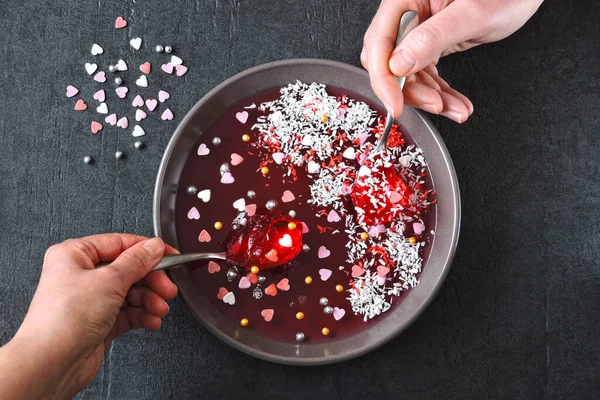 Male and female hand with spoons eat red marmalade from the bowl, decorated for Valentine\'s Day.