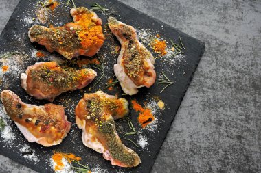 Çiğ tavuk kanatları, baharatlarla marine edilmiş siyah bir taş tahtada..