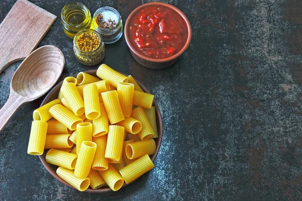 未煮熟的意大利面放在碗里 番茄酱和调味品 木叉和勺子 用番茄酱烹调意式面食 顶部视图 — 图库照片