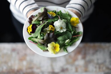 İnce bir kızın ellerinde bir tabak salata. Çiçek salatası yiyen güzel bir kız. Diyet konsepti. Sağlıklı gıda konsepti.