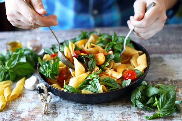 Hands of the chef mix the pasta in a pan. One pan pasta. Vegan pasta with basil. Selective focus. Macro.