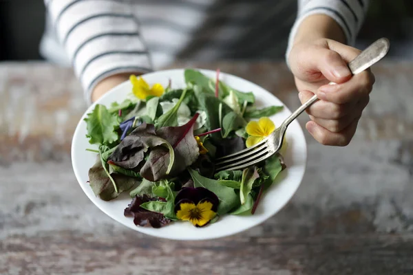 İnce bir kızın ellerinde bir tabak salata. Çiçek salatası yiyen güzel bir kız. Diyet konsepti. Sağlıklı gıda konsepti.