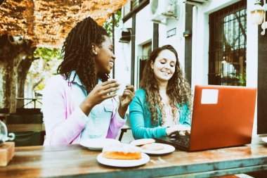 Bir kafe önünde laptoplu ve cep telefonlu iki genç kadın arasında iş görüşmesi..