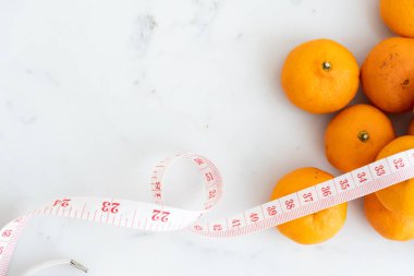 Beyaz mermer yüzeyde ölçü bandıyla sarılmış turuncu. Meyve ve besin ve diyet gıdası kavramı.