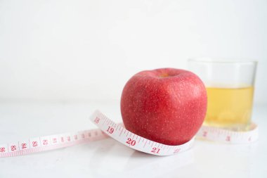 Elma ve elma suyu beyaz mermer yüzeyde ölçü bandıyla sarılmış. Meyve ve besin ve diyet gıdası kavramı.
