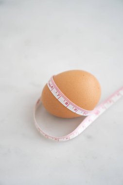 Beyaz mermer yüzeyde ölçü bandıyla sarılmış yumurta. Beslenme ve diyet gıda kavramı.