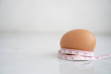 Beyaz mermer yüzeyde ölçü bandıyla sarılmış yumurta. Beslenme ve diyet gıda kavramı.