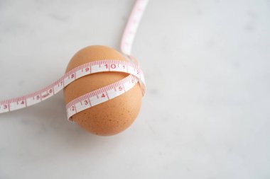 Beyaz mermer yüzeyde ölçü bandıyla sarılmış yumurta. Beslenme ve diyet gıda kavramı.