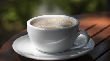 Kahve fincanı ve çay tabağı, fincandaki kahve ahşap masa ve doğa yeşili arka plan..  