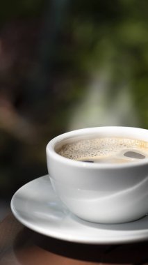 Kahve fincanı ve çay tabağı, fincandaki kahve ahşap masa ve doğa yeşili arka plan..  