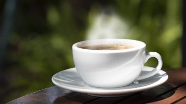 Kahve fincanı ve çay tabağı, fincandaki kahve ahşap masa ve doğa yeşili arka plan..  