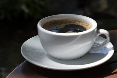 Kahve fincanı ve çay tabağı, fincandaki kahve ahşap masa ve doğa yeşili arka plan..  