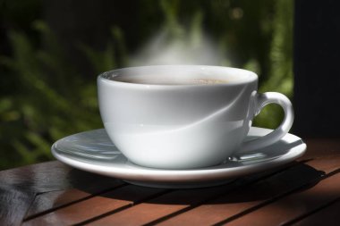 Kahve fincanı ve çay tabağı, fincandaki kahve ahşap masa ve doğa yeşili arka plan..  