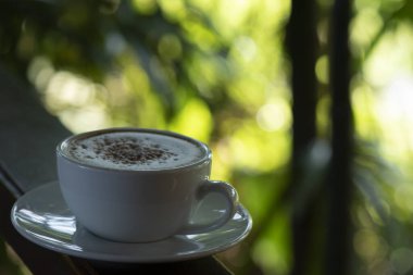 Kahve fincanı ve çay tabağı, fincandaki kahve ahşap masa ve doğa yeşili arka plan..  