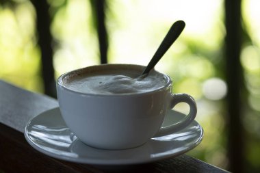 Kahve fincanı ve çay tabağı, fincandaki kahve ahşap masa ve doğa yeşili arka plan..  