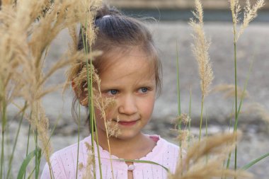 Beyaz bluzlu küçük bir kız ve gölün arka planındaki sazlıklar arasında tasarlanmış bir bakışla