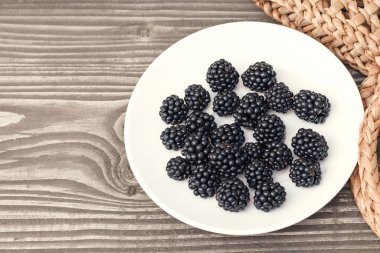 Ripe blackberries on a white plate on a wooden table background