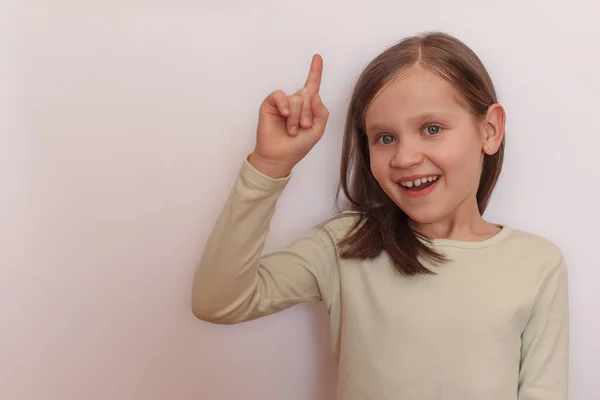 Mała Uśmiechnięta Dziewczynka Jasnym Swetrze Jasnym Tle Podniosła Rękę Pokazała — Zdjęcie stockowe