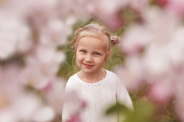 穿着白衬衫的金发小女孩正聚精会神地看着穿过花朵拍到的草丛 — 图库照片
