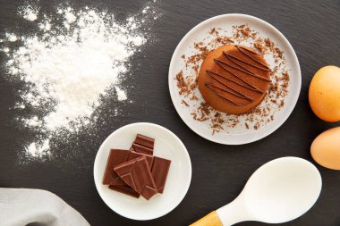 Çikolatalı Moelleux keki ya da içi rendelenmiş çikolata, un, yumurta, çikolata parçaları ve peçeteyle dolu gri bir tabakta erimiş kek. Düz yatıyordu.