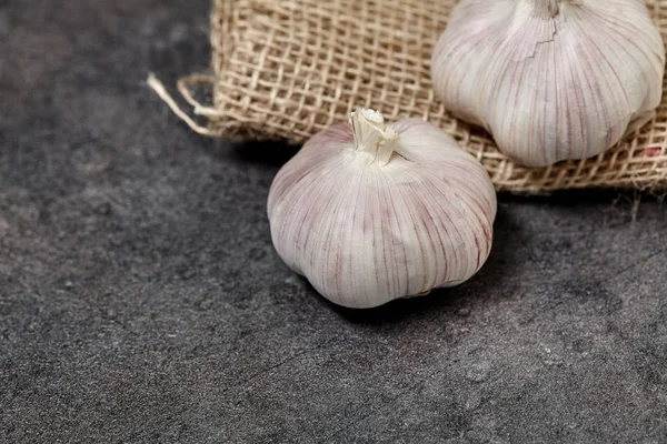 Garlick on sackcloth and black wooden table in kitchen. Food preperation for cooking. — Stock Photo, Image