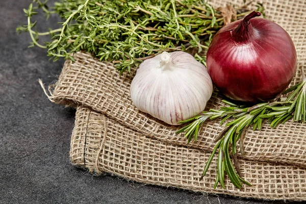 Garlick and red onion on sackcloth and black wooden table in kitchen. Food preperation for cooking. — Stock Photo, Image