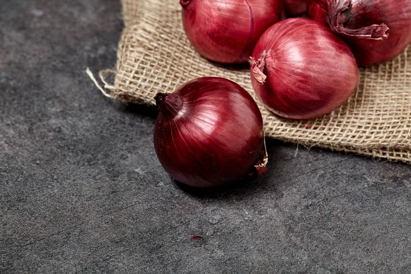 Red onion on sackcloth and black wooden table in kitchen. Food preperation for cooking. — Stock Photo, Image