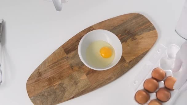 Romper el huevo en un bol sobre una mesa blanca. De cerca. . — Vídeos de Stock