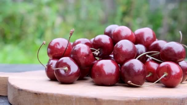 Ripe red cherry berry on natural green background and wooden table. Slow motion close up. — Stockvideo