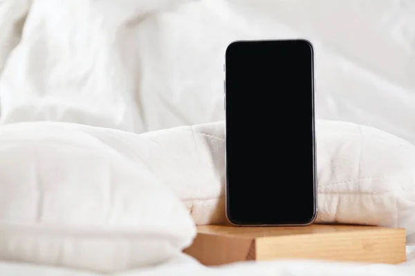 Yatak odasındaki beyaz yatakta siyah akıllı telefon. Kapat.. — Stok fotoğraf