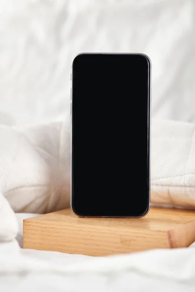 Yatak odasındaki beyaz yatakta siyah akıllı telefon. Kapat.. — Stok fotoğraf