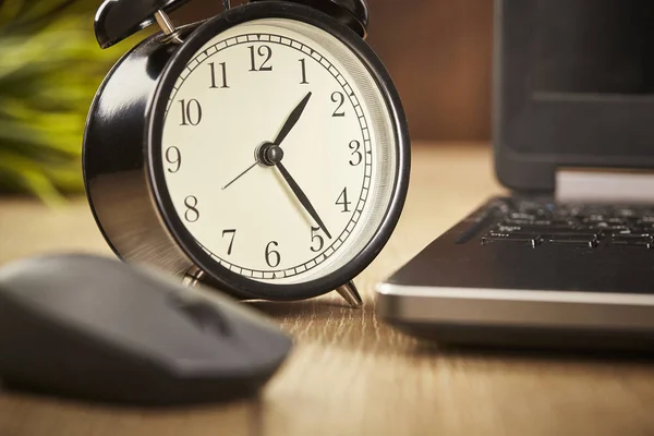 Alarm clock and laptop on wooden background. Close up.