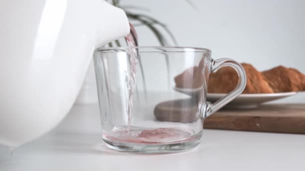 Verter té caliente en una taza de vidrio sobre una mesa de cocina blanca. De cerca. . — Vídeos de Stock