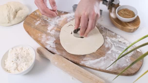 Mains féminines découpant des formes de pâte roulée avec des coupeurs de coeur sur la table blanche. Gros plan . — Video