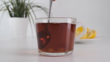 Şekeri şeffaf cam bardakta çay ile karıştırıp beyaz masaya koy. Yavaş çekim.