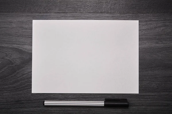 Leeres weißes Papier mit Stift auf einem schwarzen Holztisch. Nahaufnahme. — Stockfoto