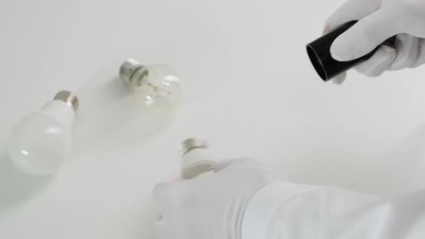 Male hands twisting electrical saving lightbulb on white table. Close up. — Stock Video