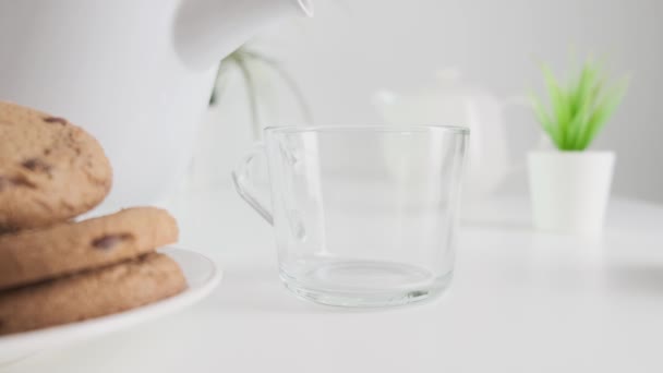 Versare il latte nel bicchiere sul tavolo della cucina con i biscotti. Alimenti sani a base di latticini. Da vicino. . — Video Stock