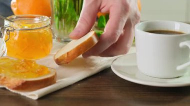 İnsan eli tostun üzerine tereyağı sürerek bir fincan kahveyle kahvaltı yapıyor. Xcose yukarı.