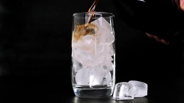 Verter Cola com cubos de gelo em vidro sobre fundo preto. Fechar . — Vídeo de Stock