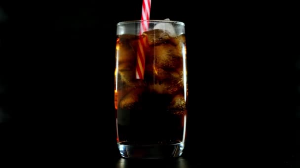 Mettre la paille dans le cola avec des glaçons en verre sur fond noir. Gros plan . — Video