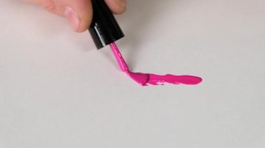 Female hands draw line on white with pink nail paint. Close up.