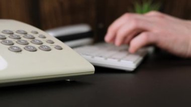 Hands of a man is using a computer, typing on keyboard, call the phone. Close up.