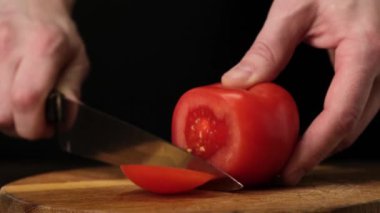 Slicing fresh tomato on wooden the cutting Board. Black background. Close up.