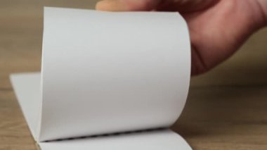 Hand flipping empty notebook pages on a wooden table. Close up