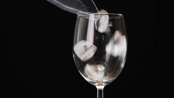 Pour ice cubes into a glass on black background. Close up. — Stockvideo