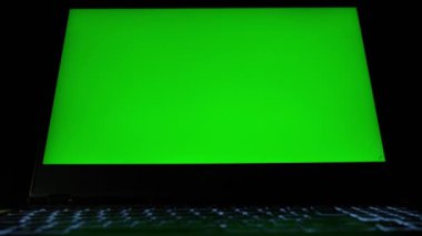 Laptop with green screen. Dark office. Close up.