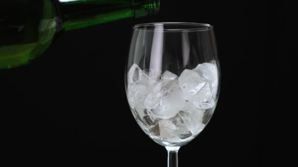 Pouring white wine in glass with ice cubes on black. Close up. — 비디오