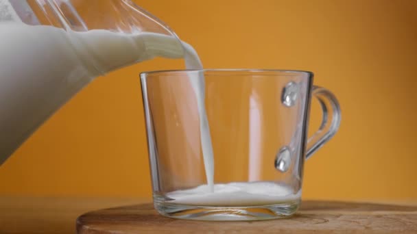 Cerrar Leche vertida en vidrio del frasco sobre tabla de madera con fondo de color. De cerca. . — Vídeos de Stock